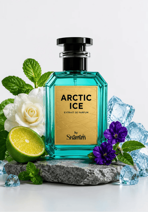 A bottle of Shamm Arctic Ice Extrait de Parfum centered on a gray stone slab, surrounded by mint leaves, a white rose, purple flowers, a lime half, and clear ice cubes against a clean white background.