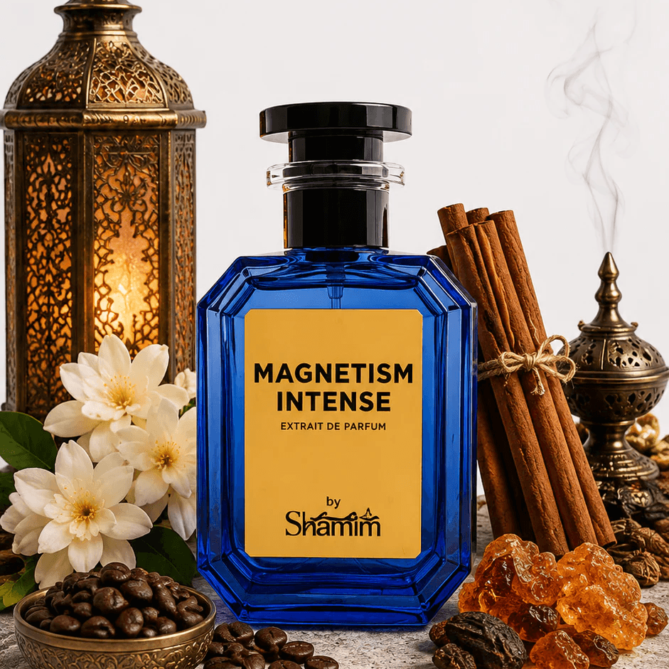 A blue glass perfume bottle labeled 'MAGNETISM INTENSE' by Shamin, styled on a stone slab with cinnamon sticks, coffee beans, white flowers, amber crystals, and brass lanterns against a light gray background.