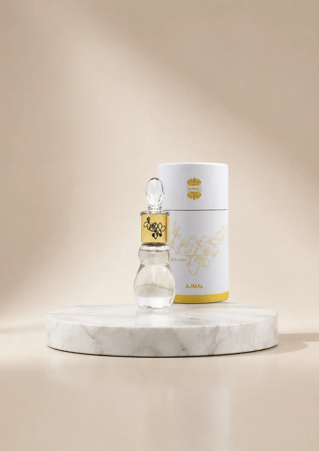 A small clear glass dropper bottle with a gold label stands in front of a white cylindrical product box with gold detailing, both placed on a round white marble pedestal against a warm beige studio background.