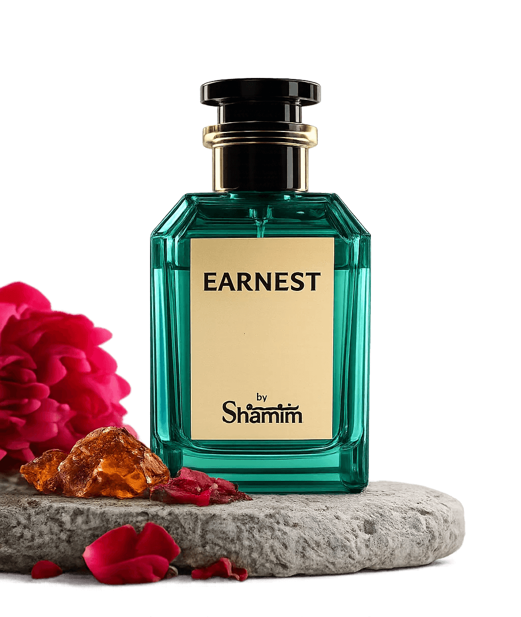 A faceted teal-green perfume bottle labeled 'EARNEST by Shamim' with a cream label and black cap, displayed on a stone slab with red flowers and amber stones against a black background.