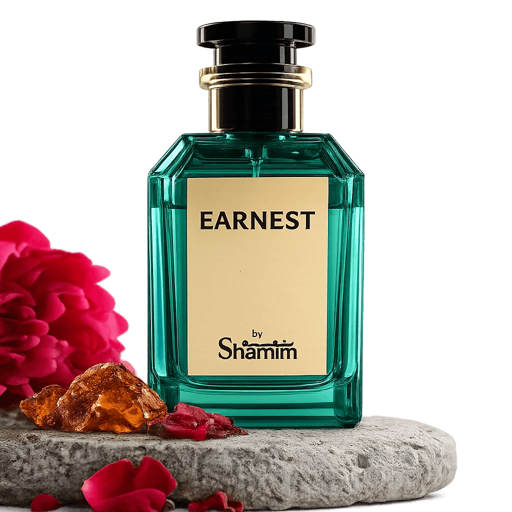 A faceted teal-green perfume bottle labeled 'EARNEST by Shamim' with a cream label and black cap, displayed on a stone slab with red flowers and amber stones against a black background.