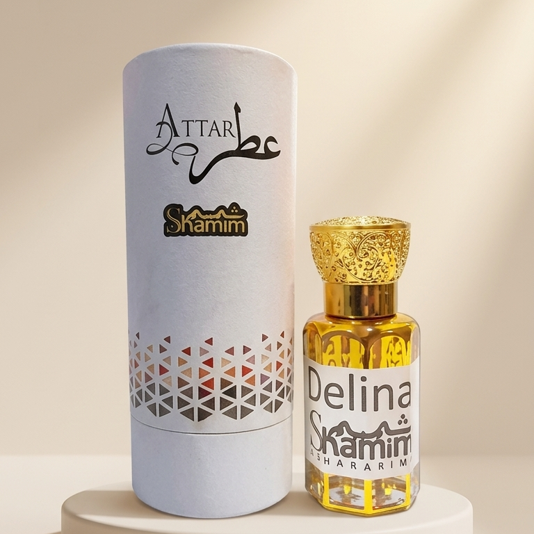 A small bottle of Attar Shamim Delina perfume with a textured gold cap stands next to its tall white cylindrical packaging box on a round pedestal. The background is a warm beige with soft diagonal shadows.