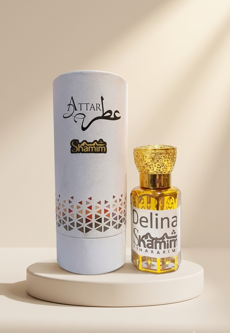 A small bottle of Attar Shamim Delina perfume with a textured gold cap stands next to its tall white cylindrical packaging box on a round pedestal. The background is a warm beige with soft diagonal shadows.