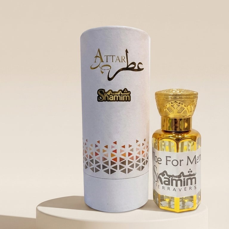 A small bottle of Attar Shammim perfume oil with a gold cap stands next to its white cylindrical packaging box on a round white pedestal. The box features gold Arabic calligraphy reading 'Attar' and 'Shammim', with a geometric pattern near the bottom.