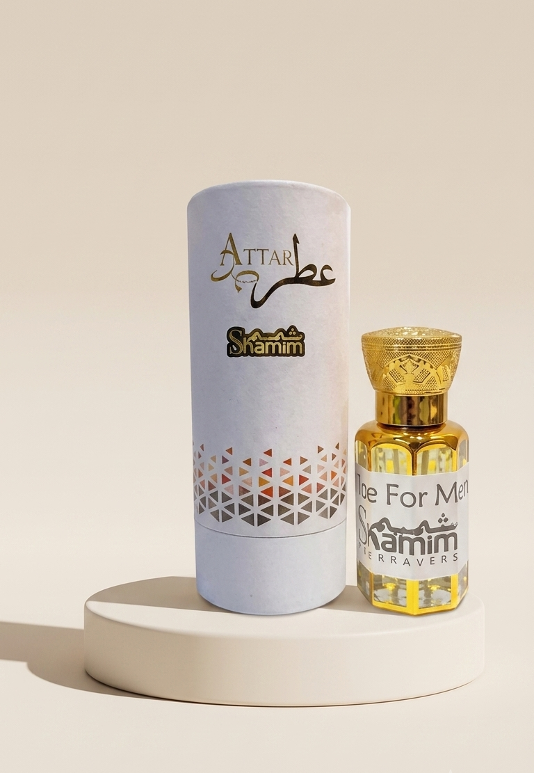 A small bottle of Attar Shammim perfume oil with a gold cap stands next to its white cylindrical packaging box on a round white pedestal. The box features gold Arabic calligraphy reading 'Attar' and 'Shammim', with a geometric pattern near the bottom.