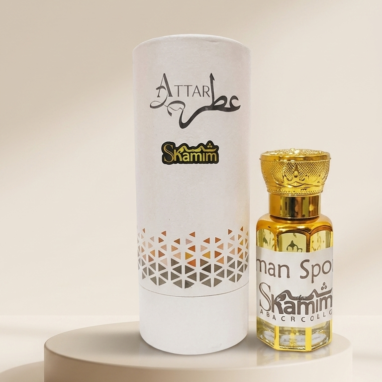 A small ornate bottle with a gold cap and gold-toned liquid beside a tall white cylindrical box, both printed with the brand name Attar Scamim, displayed on a round beige pedestal against a warm cream background.