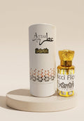 Attar Skamin perfume bottle with golden liquid and cap next to its white cylindrical packaging box, displayed on a round beige pedestal against a warm beige background.