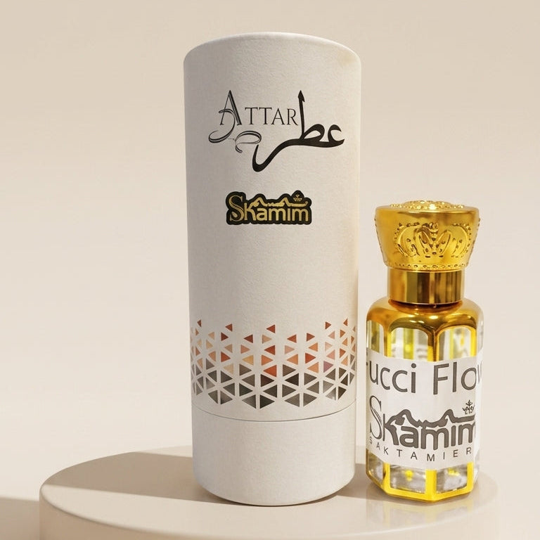 Attar Skamin perfume bottle with golden liquid and cap next to its white cylindrical packaging box, displayed on a round beige pedestal against a warm beige background.