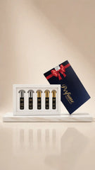 A perfume gift set featuring four small black spray bottles with gold caps in a white tray, alongside a dark navy blue gift box with a red ribbon and gold 'Perfume' lettering, set on a marble-like base against a warm beige background.
