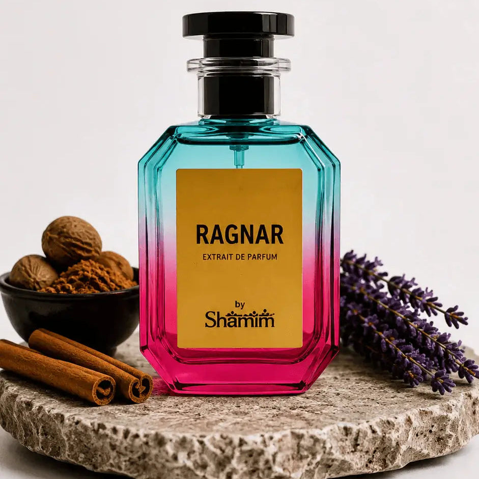 A faceted glass perfume bottle with a black cap, featuring a yellow label that reads 'RAGNAR EXTRAIT DE PARFUM by Shamim'. The bottle has a vibrant blue-to-pink gradient.