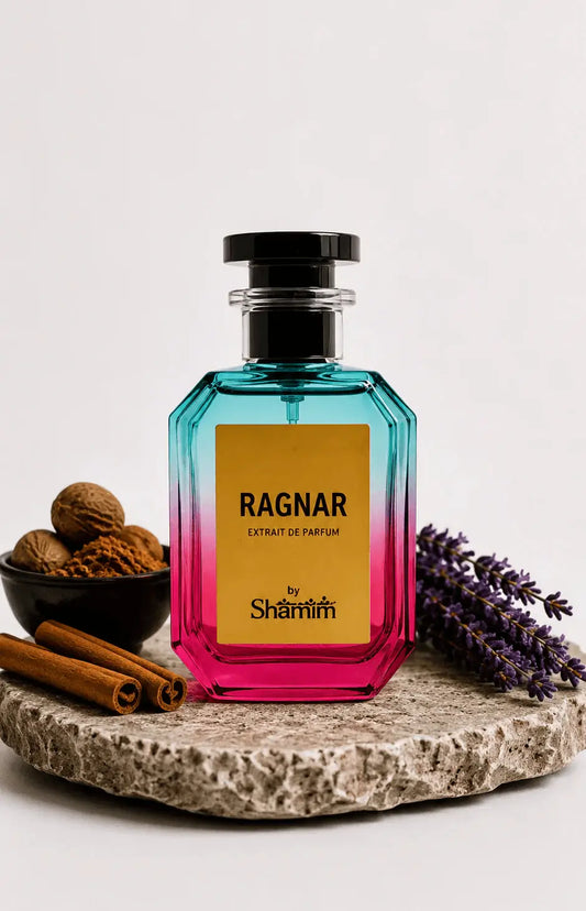 A faceted glass perfume bottle with a black cap, featuring a yellow label that reads 'RAGNAR EXTRAIT DE PARFUM by Shamim'. The bottle has a vibrant blue-to-pink gradient.