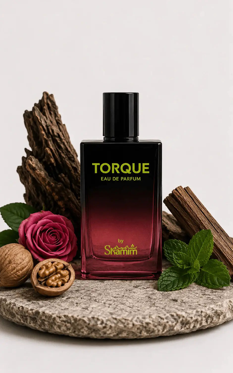 A bottle of Torque Eau de Parfum by Skaramell, featuring a black-to-deep-red gradient glass bottle with gold lettering, styled on a stone plate with a rose, walnuts, cinnamon, and mint leaves against a light gray background.